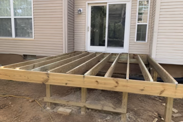 Backyard deck remodel under construction with exposed wooden framing and joists beside a residential home.