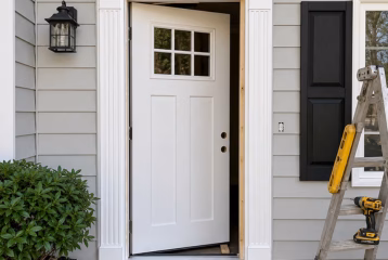 Residential door installation in progress with a new white entry door, unfinished door frame, and construction tools at the entrance.