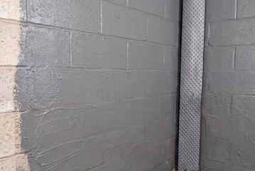 Waterproof cementitious coating applied to a basement cinder block wall alongside an interior French drain pipe and dimple board membrane.