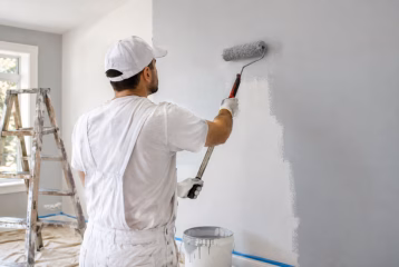 Professional painter applying fresh interior wall paint with a roller in a residential room.