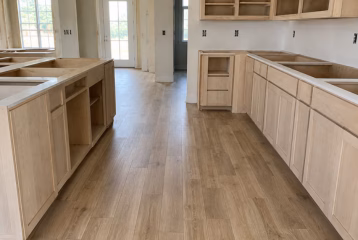 New kitchen flooring installed during construction beside unfinished custom cabinetry