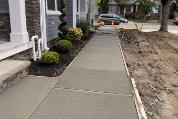 Residential concrete sidewalk installation with freshly poured walkway, wooden forms, and prepared construction area