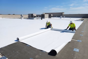 Workers installing TPO roofing membrane on a commercial flat roof